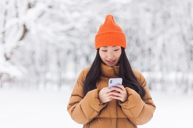 young asian woman, in the park on a date, waiting, on a winter snowy day, online uses the phone