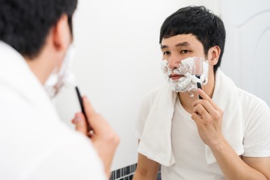 man using razor to shaving his face with cream foam in the bathroom mirror