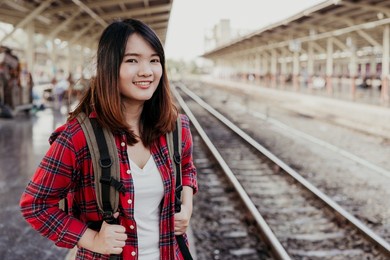 young asian woman backpacker traveler walking alone at train station platform with backpack. asian woman waiting train at train station for travel. summer holiday traveling or young tourist concept.