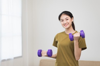 attractive asian young fitness woman lifting dumbbell weights workout at home in living room. fresh feeling female training and exercise wearing sport wear fit body.