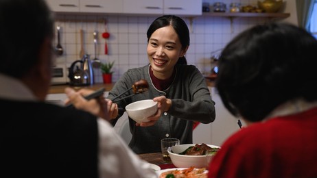 selective focus of a thankful asian daughter in law offering food to her elderly father and mother with chopsticks while having family reunion meal during spring festival