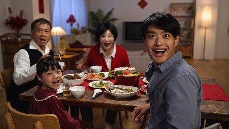 rear view surprised asian father and daughter turning to look at camera with other family members, showing wonder as someone walking near dinner table with delicious food