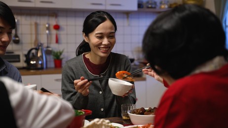 over shoulder shot with selective focus smiling asian daughter in law receiving food from her senior mother in the bowl at dinner table on the eve of chinese new year