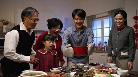 smiling asian father serving hot soup on the dining table and posing with folded arms, feeling proud of his cooking. preparing food for family on chinese new year's eve