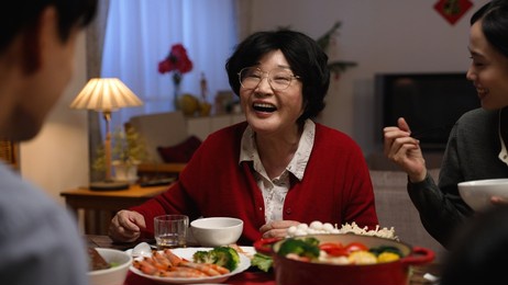 selective focus of a cheerful senior woman grandmother talking with hand gestures while chatting with her adult son at dinner table during family reunion meal at home