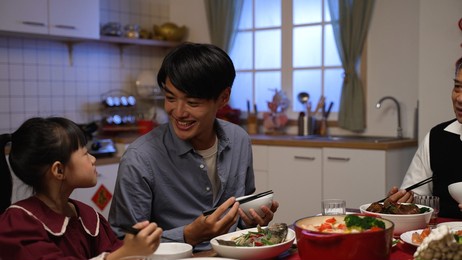 happy chinese father talking to his daughter while enjoying big meal with family. mixed generation having chinese new year dinner at home.