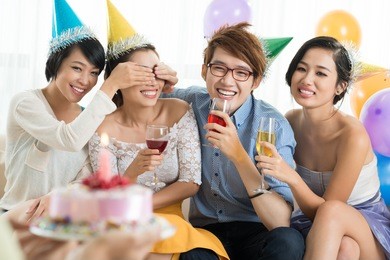 young people covering eyes of their friend to give her a birthday cake