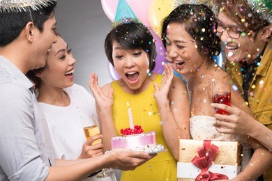 friends presenting a birthday cake to the astonished girl