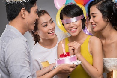 blindfolded birthday girl receiving a cake from her friends