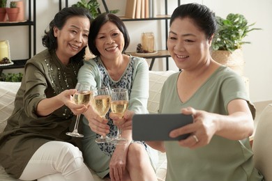 positive senior woman taking selfie with friends when they are toasting with wine glasses