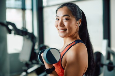 happy asian sportswoman lifting dumbbells during strength training in a gym and looking at camera.