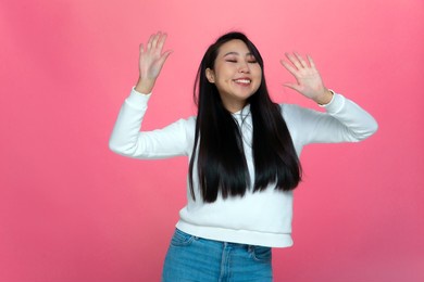overjoyed asian young girl dancing listen to music. happy female having fun enjoy party on modern pink studio background