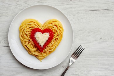 heart shaped spaghetti with tomato sauce and parmesan cheeses on white plate with white wood background.romantic vegetarian art food idea for valentine's dinner.top view.copy space