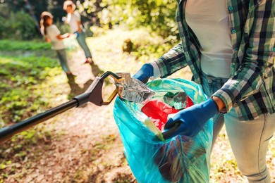 volunteers cleaning up the park, a woman is putting trash in a garbage bag and some kids are helping her, environmental protection concept