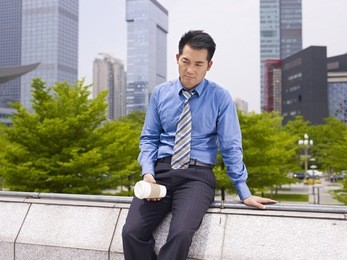 frustrated asian business executive sitting in city park.