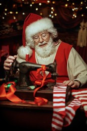 christmas traditions and fairy tales. santa claus sews christmas stockings in his workshop preparing for giving presents to children. santa's workshop. 