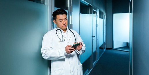 sad asian doctor, in the corridor of the clinic uses the phone, a depressed man, surfing the internet online