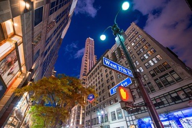 fifth avenue street sign at night with manhattan buildings on background.