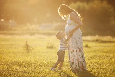 small boy kissing belly of his pregnant mother outdoors