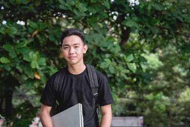 a young college student with a backpack and carrying his laptop while outside the school campus.