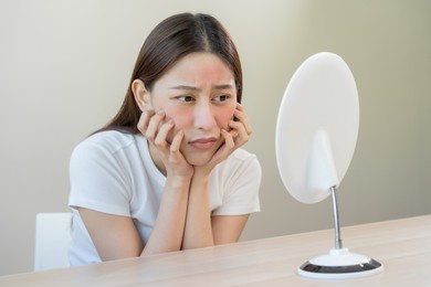 dermatology, puberty asian young woman, girl looking into mirror, allergy presenting an allergic reaction from cosmetic, red spot or  rash on face. beauty care from skin problem by medical treatment.