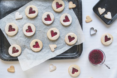 flat lay image of hear shaped linzer jam and jelly filled cookies. baking treats concept including jam, cookie cutters, icing sugar and baking sheets in top down view. romance and love food concept.