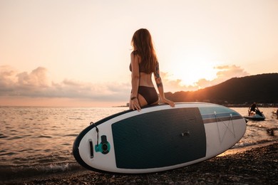 sup boarding. a tanned young woman with a tattoo poses standing with a sup board. back view. the concept of active lifestyle and surfing.