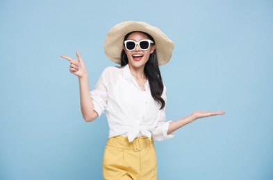 young elegant beautiful asian woman dressed in summer clothes smiling and pointing to empty copy space isolated on blue background.