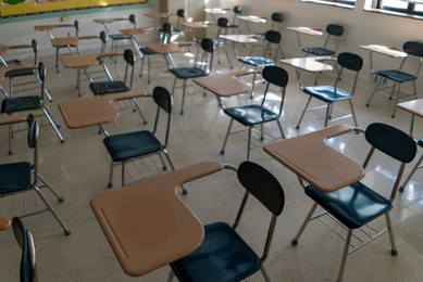 desks in empty dark high, middle, or elementary school classroom with light coming through windows.
