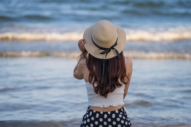 back side of young asian girl wearing sun hat on the tropical beach with blue sea water background, close up, vietnam