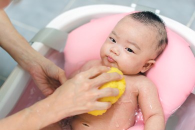 asianmother give a bath newborn baby in a tiny bathtub in bathroom.