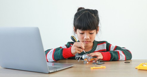 the little girl asian building robotic car in science lesson in the house . which increases the development and enhances learning skills gifted brilliant children working with technology.