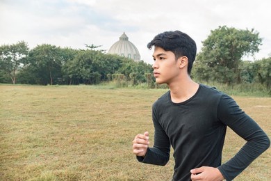 a young asian man running at a relaxed and casual pace at an open field. a warmup run.