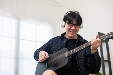 lifestyle concept. young asian musician playing guitar in living room at home on this weekend. relaxing with song and music. asian man having fun playing acoustic guitar