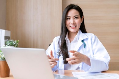 professional attractive asian female doctor diagnosis talking and looking to camera in video conference ,positive doctor waving and having online doctor examine consultation on digital tablet laptop