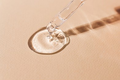 transparent body serum flowing from a glass pipette front view.cosmetic product close-up on a beige background.
