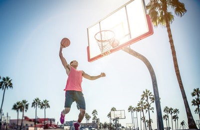 young players playing basketball at the court in venice beach, california. professional street ballers having fun performing tricks and huge slam dunks
