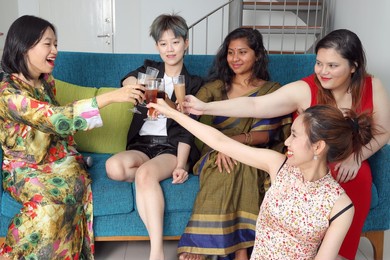 young southeast asian woman group talk celebrate sing making funny mocking faces expression drinking cheering cheers on blue living room sofa