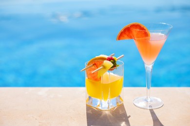 two glasses of cocktails with fresh fruits by the pool