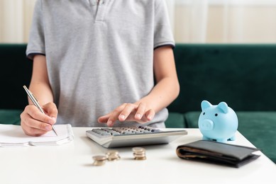 kid teen boy counting money and taking notes, saving money in a piggy bank. learning financial responsibility and projecting savings. concept of finance, business, investment. lessons in mindfulness.