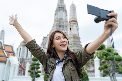 asian woman backpacker use mobile phone selfie, take picture in city. young girl tourist traveler travel alone on street use cellphone record vlog on holiday vacation trip in buddha temple in thailand