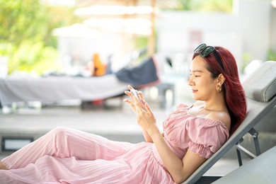 young asian beautiful woman lying in bed and checking mobile phone and enjoying social media and resting on vacation trip. woman lifestyle, relaxation and summer concept