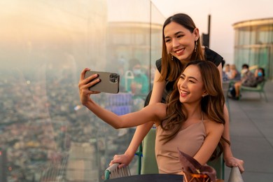 asian woman friends in meeting and using smartphone selfie together at skyscraper rooftop restaurant in metropolis at summer sunset. female friend enjoy outdoor lifestyle activity in the city at night