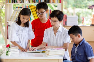 a group of asian student kid reading  book with female teacher in school library with shelf of books in background, asian kid education summer classroom concept thailand 