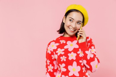 smiling happy woman of asian ethnicity 20s wear red knitted sweater beret talk speak on mobile cell phone conducting pleasant conversation isolated on plain pastel pink background studio portrait.