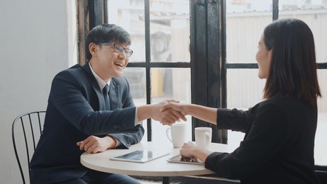 happy two asian young businessman and woman shaking hands greeting before meeting or negotiation with digital tablet sitting on desk cafe, businesspeople discussion planning and smile lunch