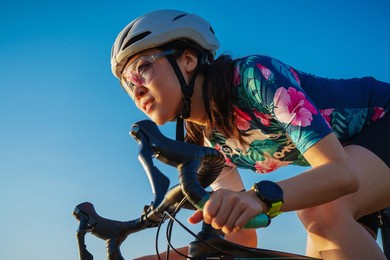 close up asian woman with athletic body shape in protective helmet and glasses riding bicycle on blue sky 
