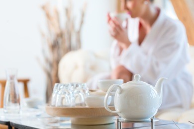 woman in bath robe drinking tea in wellness spa relaxation room