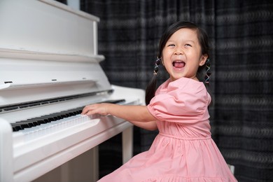 asia girls wearing dress look at camera and smile playing white piano. enjoying time practicing music at school. musician kid feeling happy and relax during class. education and learning concept