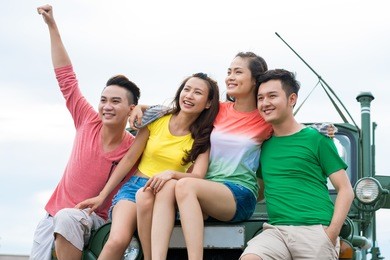 group of cheerful young people sitting on the car hood and enjoying the view